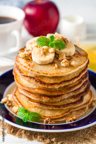 Pancakes with banana, honey, walnuts and mint on plate.
