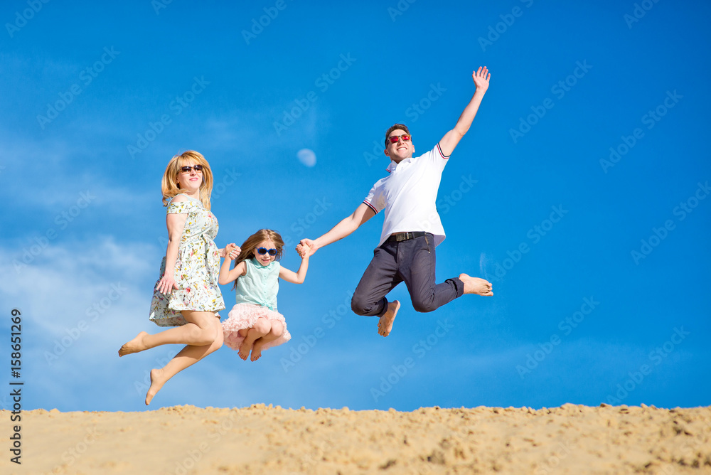 Beautiful happy family walking, running, jumping, having fun along the sand on the beach against the background blue sky in summer vacation Beautiful happy family walking, running, jumping, having fun along the sand on the beach against the background blue sky in summer vacation