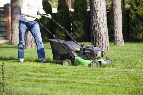 the man mowing lawn in the backyard of his house. Lawn mowing. Green grass is mowed lawn mower