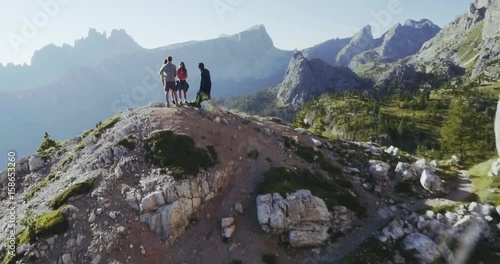 Aerial flight above people hiking along trail path in sunny day. Group of friends summer adventure journey in mountain nature outdoors. Travel exploring Alps, Dolomites, Italy. 4k drone forward video
