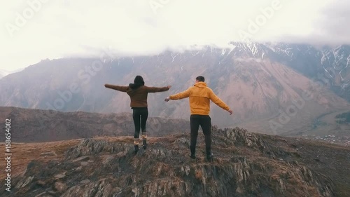 a young couple of travelers raises his arms in the background of mountains photo