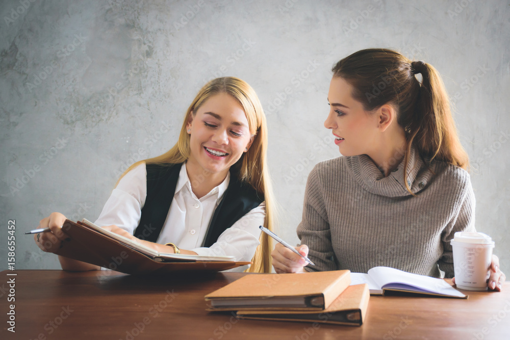Two young european business women are sitting on the table and discussing about their work or project Two young european business women are sitting on the table and discussing about their work or project