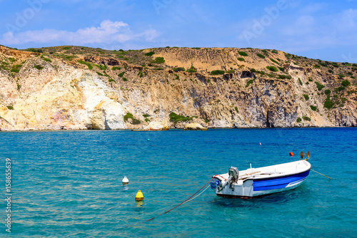 Boat in a picturesque bay with crystal blue water, Firopotamos village, Milos, Cyclades Islands, Greece.