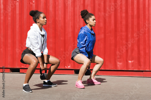 Two women exercising with kettlebell, doing squats