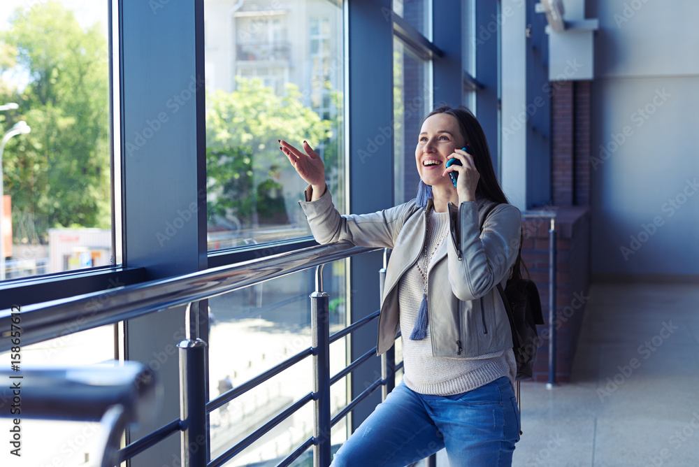 Fototapeta premium Female exited with conversation on phone while leaning on handrail