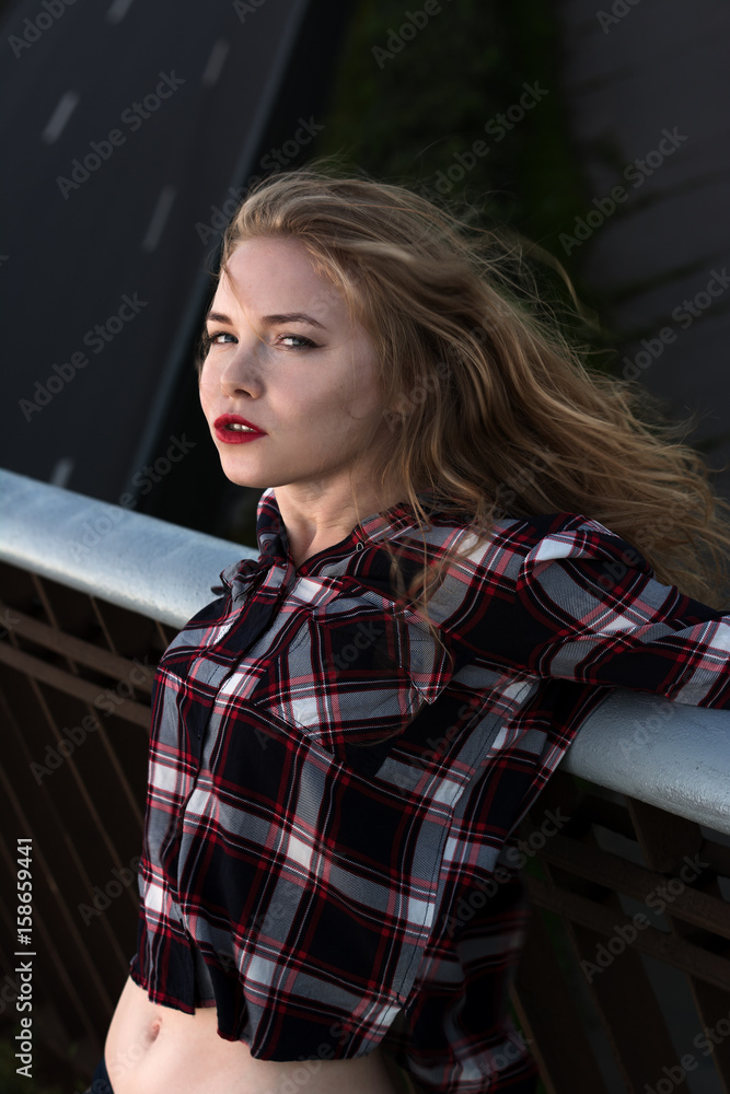 Girl in a plaid shirt. A blonde in a checked shirt on the street is leaning on a railing, close-up. Girl in a plaid shirt. A blonde in a checked shirt on the street is leaning on a railing, close-up.