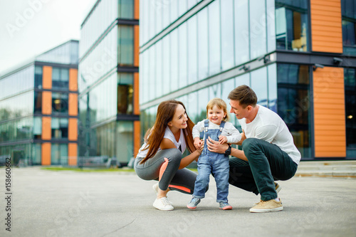 Portrait happy family of three. Young parents play with their little daughter while walking through the streets of the city.