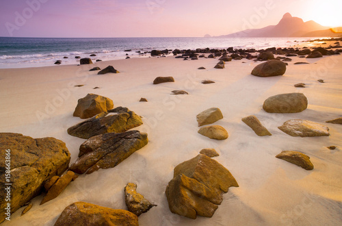 Romantic atmosphere in peaceful Sunset at Bai nhat beach Condao island-Vietnam. Taking with long exposure in the evening smooth wavy motion by Big rocks near shoreline, pink horizon with sun rays. photo