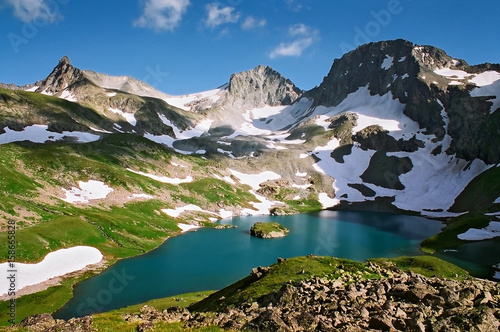 Beautiful scenic landscape of Great Imeretinskoye mountain lake (Lake of Stillness) surrounded with Caucasus mountain peaks with snow melting on slopes on sunny day at summer