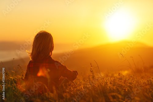 Woman sits with her back in the field and admires the sunset in the mountains. © JenkoAtaman