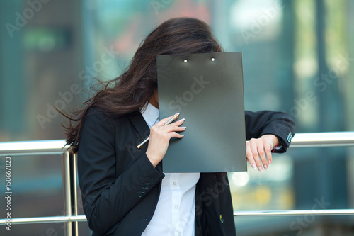 Quadro su tela Embarrassed shy young girl in suit with black folder in hands on the background