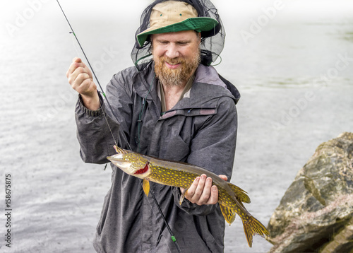 Happy fisherman holding his catch of a freshwater pike