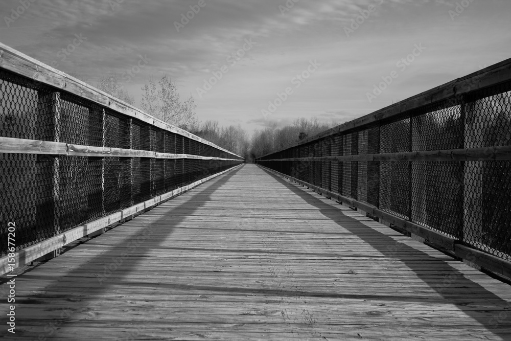 The Long Journey. Long wooden footbridge with a diminishing perspective in horizontal orientation in black and white. Wadhams to Avoca Rail Trail. Avoca, Michigan.