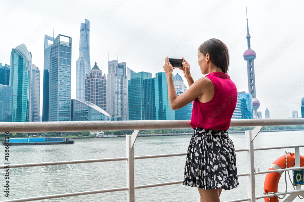 Fototapeta premium Azjatycka biznesowa kobieta robi zdjęcie telefonu panoramy Pudong podczas rejsu promem do Szanghaju w kierunku centrum dzielnicy finansowej w Chinach. Kobieta turystycznych patrząc na widok robienia zdjęć.