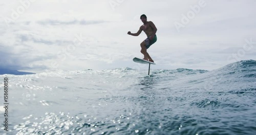 Surfer on hydrofoil surfboard riding blue ocean wave. Futuristic surfing on hoverboard