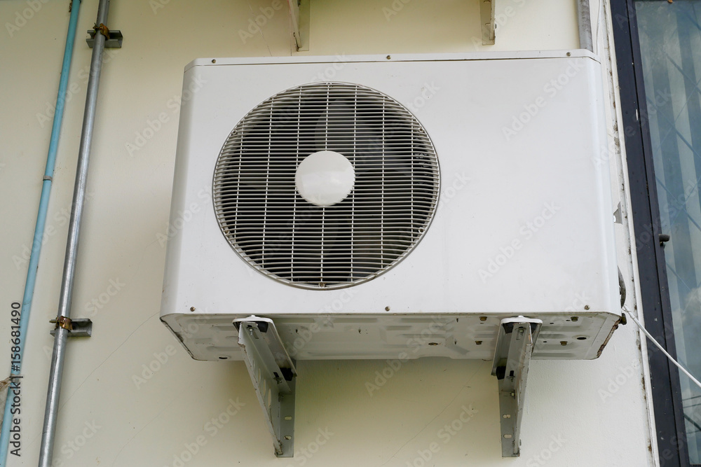 Air conditioner condenser unit at a white concrete wall Air conditioner condenser unit at a white concrete wall