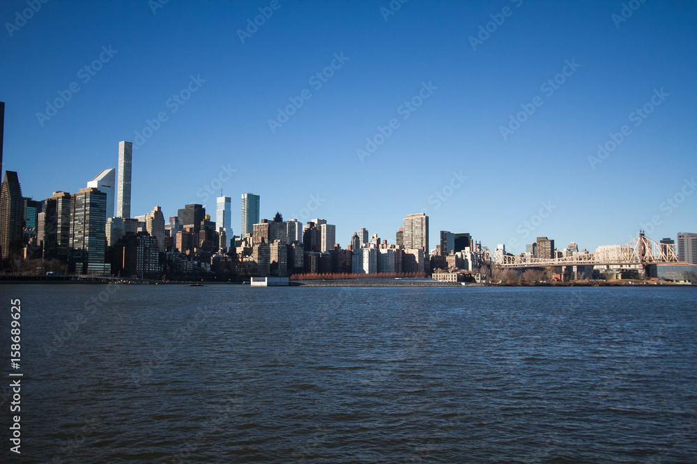 Obraz premium Buildings and bridge over river with blue sky, New York