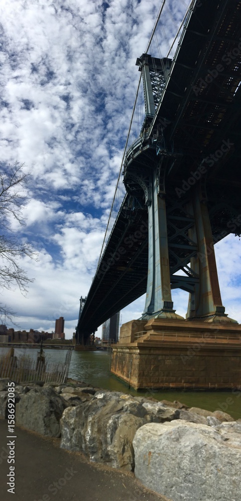 Fototapeta premium Manhattan bridge over the river and rocks at Brooklyn bridge park with cloudy sky