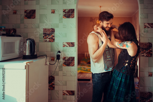 Loving couple lying in bed together. Handsome young hipster with beard and attractive woman resting at home while kissing and cuddling.