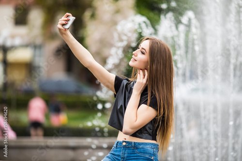 Young happy woman make selfie on the street of old town with fountain in background.