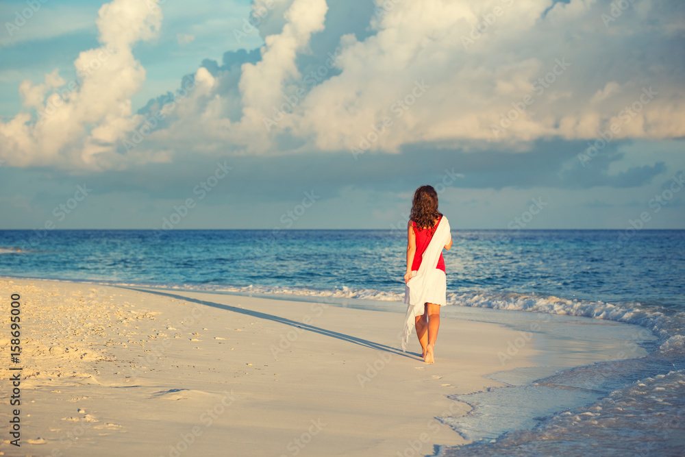 Attractive young woman walking along ocean beach at sunset Attractive young woman walking along ocean beach at sunset