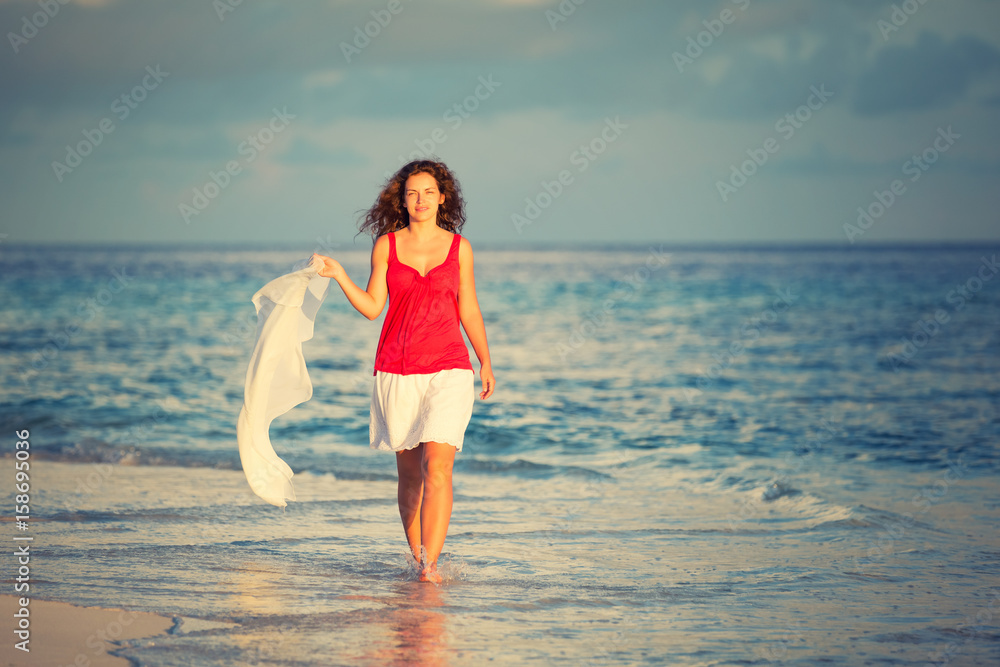 Attractive young woman walking along ocean beach at sunset Attractive young woman walking along ocean beach at sunset