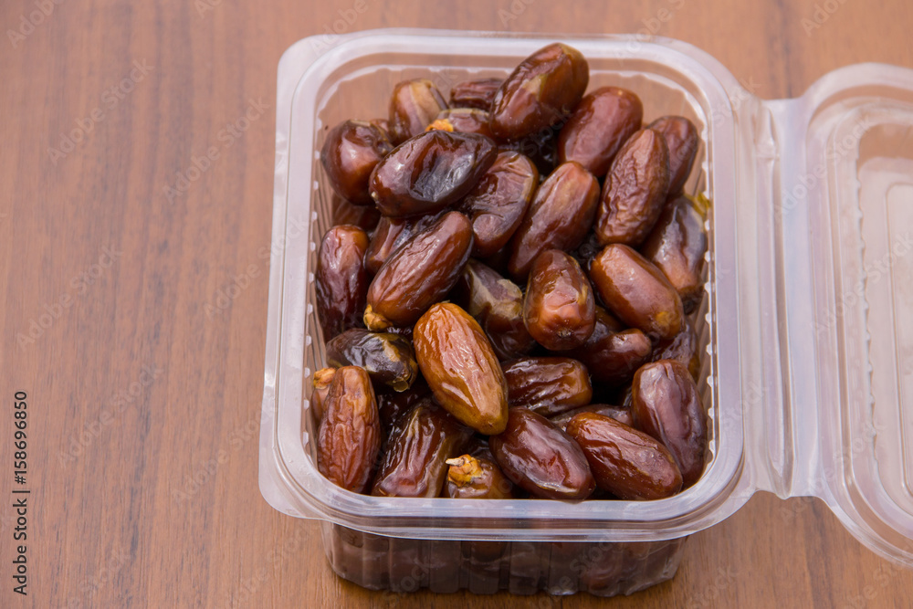 Dried date fruits in plastic container on wooden table Dried date fruits in plastic container on wooden table