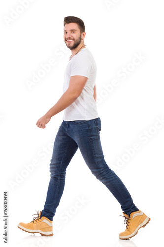 Smiling Man In Jeans And White T-shirt Is Walking Side View