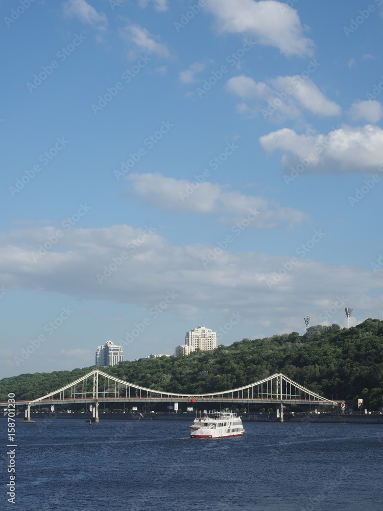 Naklejka premium A white pleasure boat with passengers aboard sailed along the center of the river in Kiev