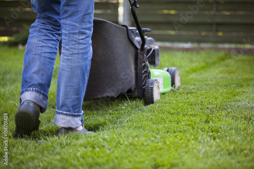 the man mowing lawn in the backyard of his house. Lawn mowing. Green grass is mowed lawn mower