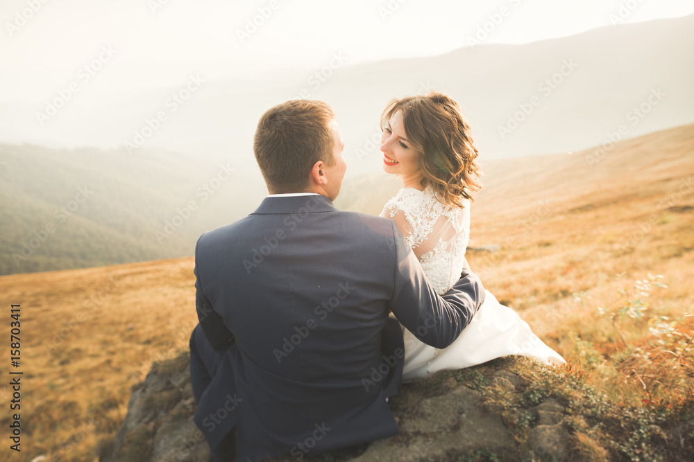 Beautiful wedding couple posing on top of a mountain at sunset Beautiful wedding couple posing on top of a mountain at sunset