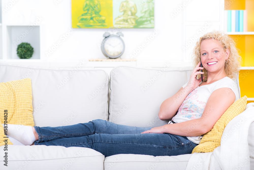 Blonde Frau liegt auf Sofa und telefoniert mit Mobiltelefon
