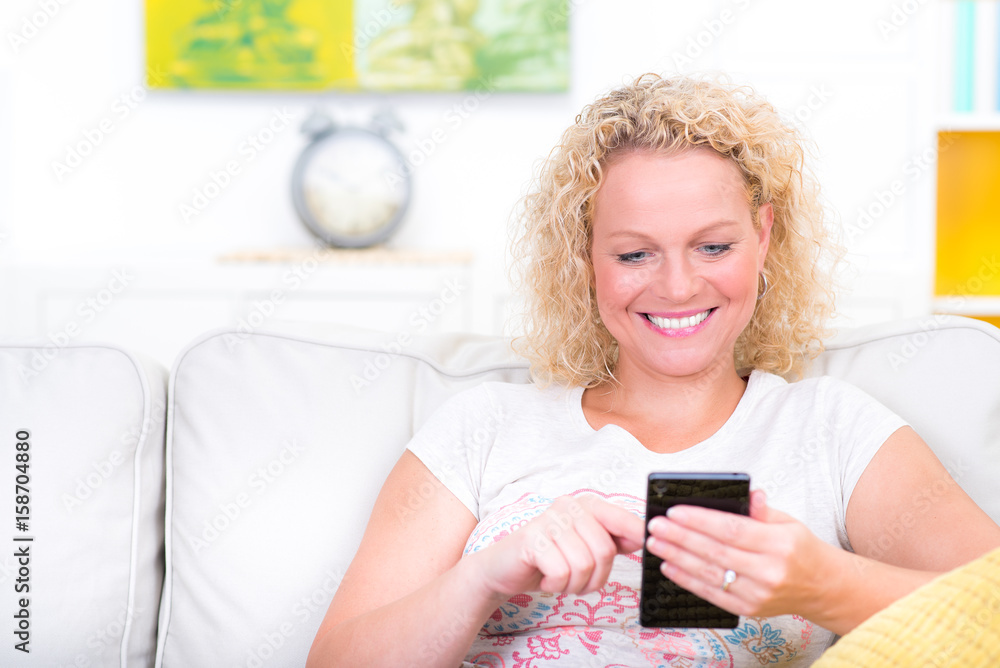 Blonde, hübsche Frau schreibt SMS auf Sofa Blonde, hübsche Frau schreibt SMS auf Sofa