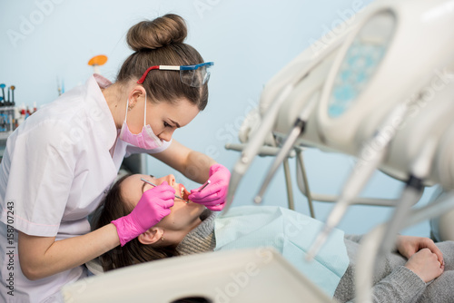 Female dentist with dental tools - mirror and probe checking up patient teeth at dental clinic office. Medicine, dentistry and health care concept. Dental equipment photo