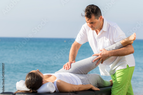 Osteopath doing hip and leg treatment outdoors on patient.