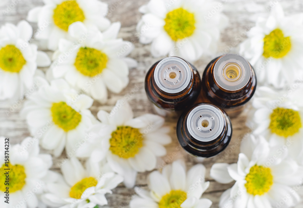 Three bottles of essential chamomile oil over wooden background. Aromatherapy and spa concept. Top view, copy space. Three bottles of essential chamomile oil over wooden background. Aromatherapy and spa concept. Top view, copy space.