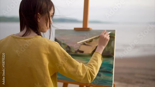 A cute and creative teenager draws a still life from nature, the canvas stands on the easel. An irascible girl draws the sea and mountains in the Impressionist style, she uses a palette with oil