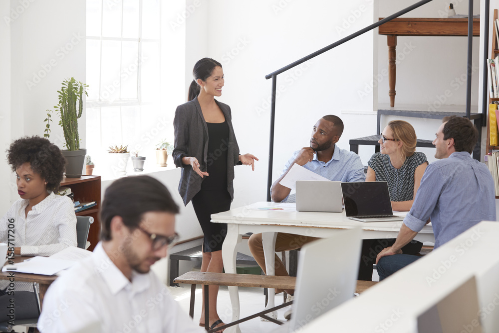 Woman talking to colleagues at a desk in open plan office