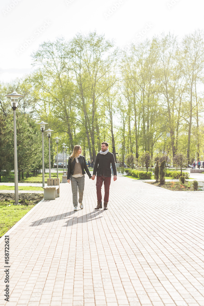 Stylish pregnancy concept - portrait of couple of hipsters husband and wife in trendy clothes walking in the city park