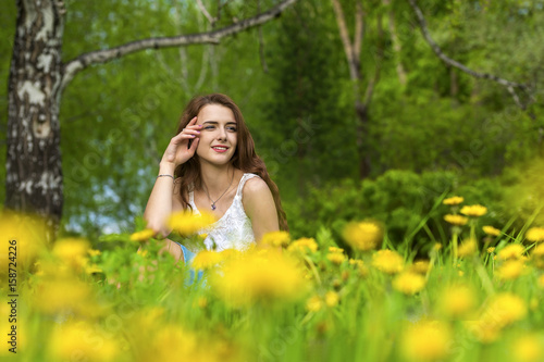 Girl with long hair sitting on the lawn with blooming dandelions