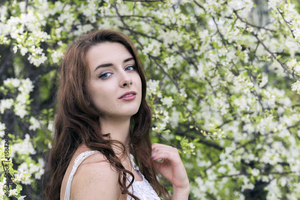 Fototapeta premium Portrait of a girl surrounded by white blossoming apple trees