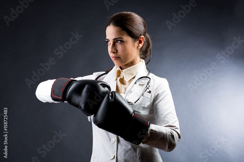 Medico donna con espressione decisa, in camice bianco, porta dei guantoni uniti che stanno ad indicare la lotta alle malattie  - sfondo bianco e nero photo