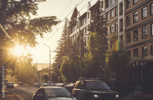 Street of the city, houses and cars in the light of the setting sun. © natavilman