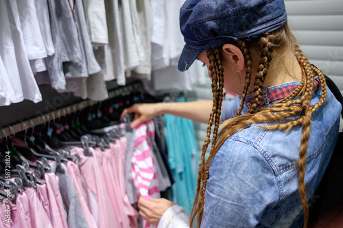 redhead girl with tress hairstyle choosing clothes in clothes store