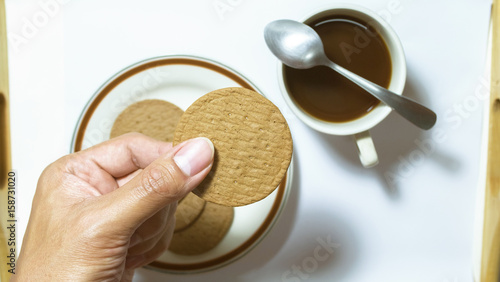 Canvas Print Hand hold brown biscuits in dish pairing with black coffee with teaspoon