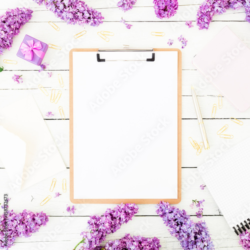 Minimalistic workspace with clipboard, purple lilac, little box and accessories on rustic wooden background. Flat lay, top view. Beauty blog concept.