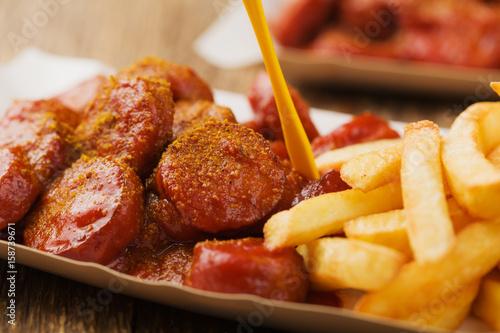 Traditional German currywurst, served with chips on disposable paper tray.