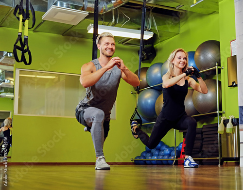 Sporty male and female doing trx straps exercises in a gym club.
