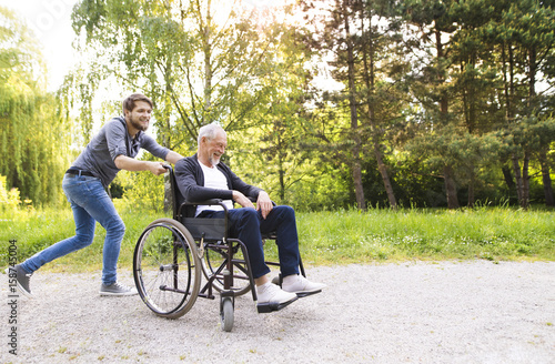 Hipster son running with disabled father in wheelchair at park.