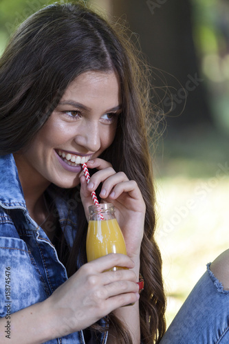 Beautiful young woman sitting in the park and drinking juice